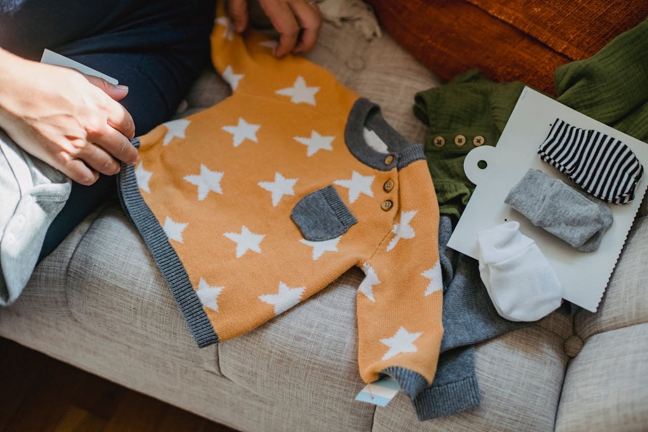 High angle of crop faceless parent sitting on sofa and showing new garment for baby